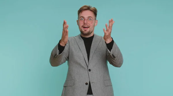 stock image Oh my God, Wow. Excited amazed winner business man raising hands in surprise looking at camera with big eyes, shocked by sudden victory. Sincere young adult guy boy isolated on blue studio background