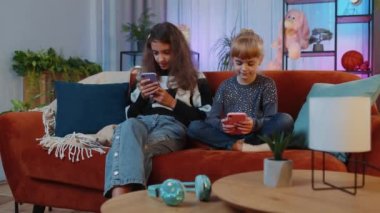 Genç kız kardeşler başarıyı kutluyor. Akıllı telefondan online alışveriş yaparken çığlıklar atıyorlar. Mutlu kardeşler çocuklar boş zamanlarını sosyal medya uygulamalarında oyun oynayarak geçirirler.