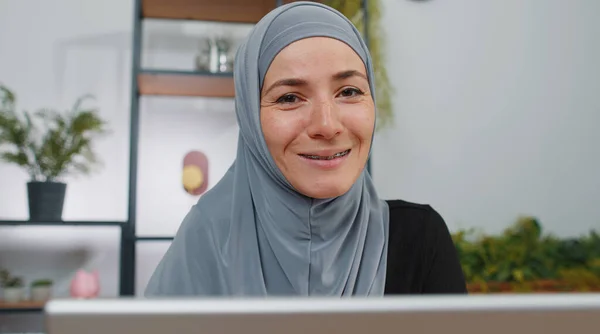 Close-up portrait face muslim business woman in hijab at office workplace, working on laptop computer. Manager freelancer girl works on notebook, sends messages makes online purchases watching movies