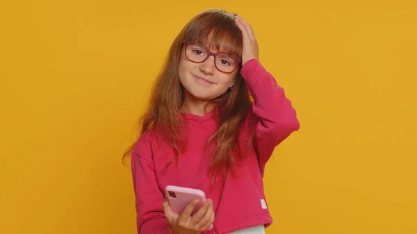 戴眼镜的幼儿在校女生用智能手机打字浏览 失去了意想不到的突然中彩票结果 黄种人背景的少女 — 图库照片