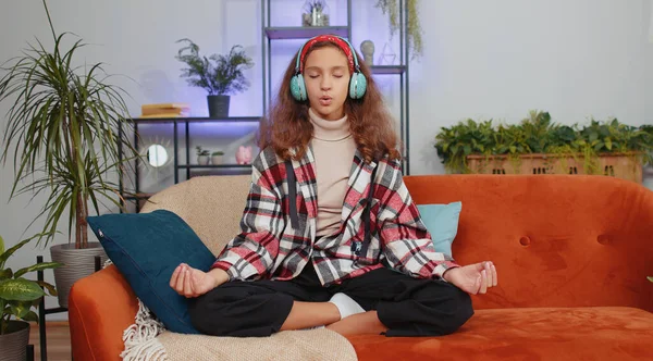 ヘッドフォンの音楽を聞いて若い未成年の少女の子供は 泥のジェスチャーの目で深く息を集中的な考えで瞑想を閉じ 部屋のソファの上に平和的な心 家にいる10代の子供 — ストック写真