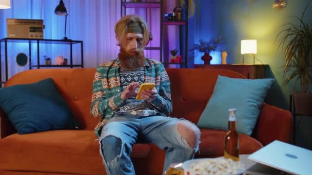 Vousatý Hippie Muž Sedící Pohovce Používá Mobilní Telefon Úsměvy Nočním — Stock video