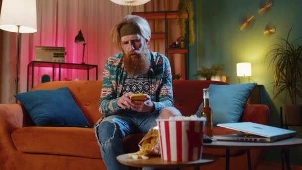 Sorgligt Skäggig Rödhårig Hippie Man Använder Smartphone Skriva Surfning Förlorar — Stockvideo