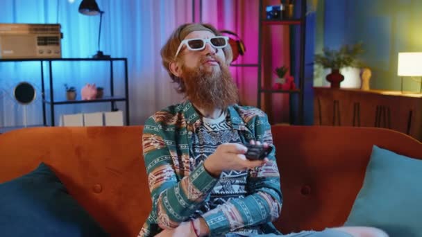 Excited Bearded Hippie Young Man Sits Sofa Use Remote Control — Stock Video