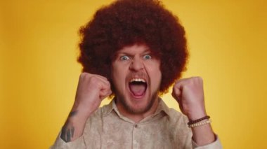 Saçları gür saçlarıyla bağıran, el kol hareketi yapan mutlu bir adam. Başarımı, kazanmamı, doğum günümü, piyango vuruşumu başarıyla tamamladım. Stüdyoda sarı arka plandaki hippi çocuk.