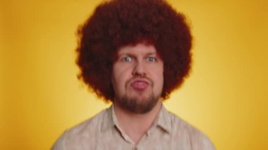 Komik, neşeli, samimi bir adam, gür afro saç stili saçı olan, şakacı, aptal yüz ifadeleri yapan ve etrafta dil göstererek sürten. Sarı arka planda izole genç yakışıklı hippi.