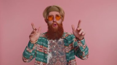 Hippi kızıl sakallı, şablon tişörtlü, müzik dinleyen, dans eden, eğlenen, el kol hareketi yapan, partide rahatlayan bir adam. Pembe arka planda güneş gözlüklü hippi.