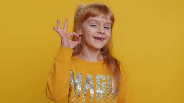 セーターを着た若い幼児の学校の女の子が承認を得て カメラを見て 正の記号のような重要なジェスチャーを示す 何か良いことを承認します ティーン女性子供子供隔離上のスタジオ黄色の背景 — ストック動画