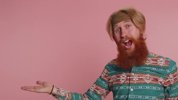 嬉皮士红头发的男人穿着花纹衬衫 竖起大拇指 指着左边的空白处 商业广告标识 文字的位置 粉红背景的嬉皮士姜人男孩 — 图库视频影像