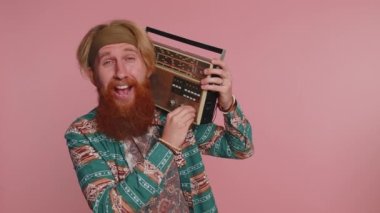 Hippi kızıl adam müziği dinlemek için retro teyp çalar, favori parçaların disko dansını yapar, eğlenir, eğlenir, klasik teknolojilerin hayranı olur. Pembe arka planda kızıl sakallı hippi.