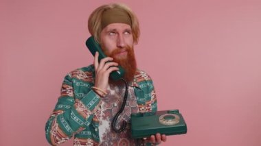 Çılgın hippi kızıl sakallı, şablon gömlekli adam 80 'lerin modası geçmiş eski telefonlardan konuşuyor, aptal suratlar yapıyor, hoş olmayan konuşmalar yapıyor. Pembe stüdyo geçmişindeki hippi kızıl çocuk.