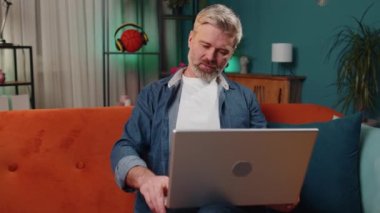 Evde kanepede oturan, dizüstü bilgisayarı açık, yakışıklı, orta yaşlı, serbest çalışan bir adam. Olgun yaşlı adam defter üzerinde çalışır, mesajlar gönderir, online alışverişler yapar, film izler, çalışır.