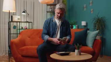 Planlama bütçesi. Zengin, orta yaşlı bir adam nakit sayıyor hesap makinesi kullanıyor ve evdeki faturaları hesaplıyor. Kazancından, kazancından, planlı tatil ve hediyeler için para biriktiren olgun yaşlı bir adam.