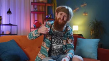 Hoşlanmamak. Sinirli adam işaret dilini gösteriyor, hoşnutsuzluğunu dile getiriyor, hoşnutsuzluğunu dile getiriyor, modern ev dairelerinde tatminsiz kötü işler yapıyor. Oturma odasında kanepede oturan hoşnutsuz hippi adam.