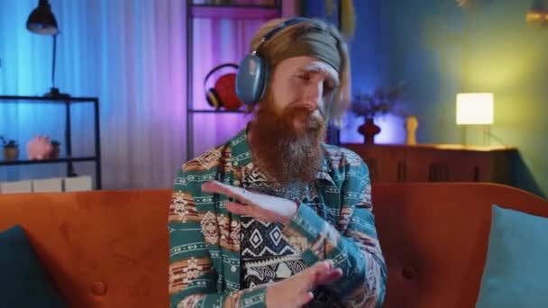 Ευτυχισμένος Χαρούμενος Hippie Γενειοφόρος Νεαρός Άνδρας Ασύρματα Ακουστικά Χαλαρώνοντας Κάθεται — Αρχείο Βίντεο