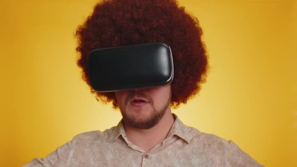 ヘッドセットヘルメットアプリを使用してシミュレーションの革新的なゲームをプレイする緑豊かなアフロヘアスタイルを持つ赤毛の髭の男 仮想現実3D 360ビデオを見る 若いです男男の子でVrゴーグル上の黄色のスタジオ背景 — ストック動画
