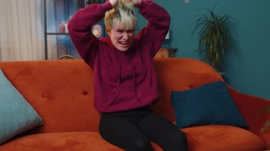 Kısa sarı saçlı korkmuş kadın stres gerginliğinden bağırıyor panik korku umutsuzluk şaşkınlık şaşkınlık jestler öfke ifade eder. Evde turuncu koltukta oturan öfkeli kız. Yaşam biçimi