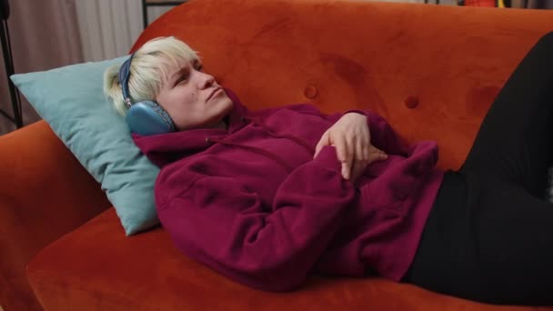 Kısa Saçlı Kablosuz Kulaklıklı Mutlu Bir Kadın Koltukta Oturup Sevdiği — Stok video