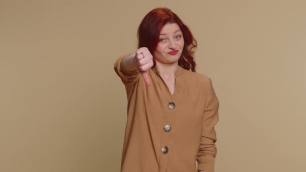 嫌いだ 親指をサインジェスチャーを示すブラウスに不幸な赤毛の女性を動揺し 嫌いな表現 若い大人の女の子 室内スタジオショットオンベージュ背景 — ストック動画