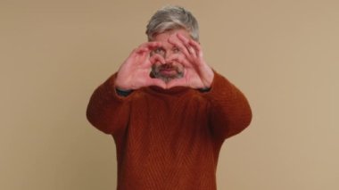 Aşık bir adam. 45 yaşında gülümseyen orta yaşlı bir adam kalp hareketi yapar. Aşk işareti iyi duygular ve sempati gösterir. Yaşlı yetişkin adam bej renkli stüdyo arka planında tek başına izole edilmiş.