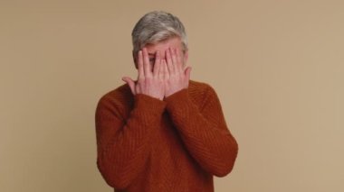 Meraklı, orta yaşlı bir adam elleriyle gözlerini kapar ve parmaklarıyla casusluk yapar, dürbün hareketlerini gizler ve uzaktan bir şeyler arar. Bej arkaplanlı yaşlı bir adam.