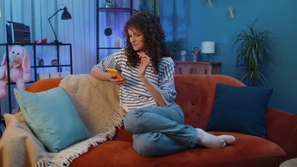 Woman Curly Hairstyle Sitting Sofa Uses Mobile Phone Smiles Night — Video Stock