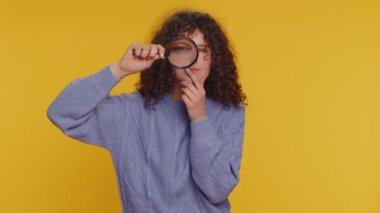 Araştırmacı bilim adamı kadın yüzünün yanında büyüteç tutan, kameraya bakan, büyük zumlanan komik gözlerle araştıran, analiz eden. Sarı stüdyo geçmişindeki kıvırcık saçlı genç kız.