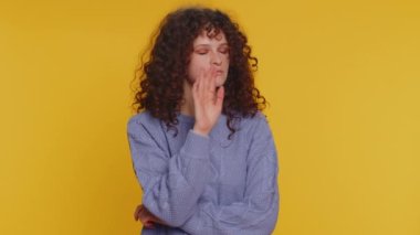 Sessiz olun lütfen. 20 yaşındaki bir kadının portresi işaret parmağını dudaklara bastırıyor. Sessiz jest işareti sır vermez. Sarı stüdyo arka planında güzel kıvırcık saçlı kız.