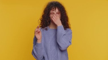 Yorgun, kıvırcık saçlı kadın gözlüklerini çıkarır, göz ağrısı hisseder, uzun çalışma saatlerinden yorgun düşmek, baş ağrısı. Mutsuz, üzgün, genç bir kız, sarı stüdyo arka planında tek başına.