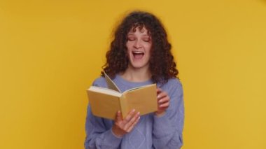 Komik masal kitabı okuyan kıvırcık saçlı mutlu kadın, boş zaman hobisi, bilgi bilgeliği, eğitim, öğrenme, çalışma, vay be. Genç kız sarı stüdyo arka planında tek başına.