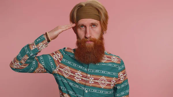 Yes sir. Subordinate, responsible serious hippie redhead man giving salute listening to order as if soldier, following discipline, obeying, expressing confidence. Hipster guy boy on pink background