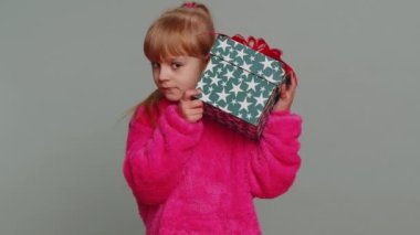 Happy toddler school girl receive, opening gift box and smiling joyfully, looking amazed satisfied with nice present unexpected birthday surprise. Teen female child kid isolated on gray background
