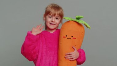 Young toddler school girl in sweater smiling friendly at camera and waving hands gesturing hello or goodbye, welcoming with hospitable expression. Teen female child kid isolated on gray background