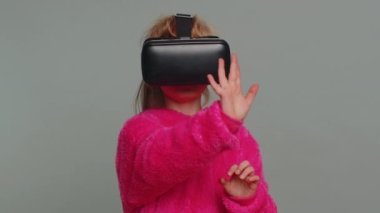 Young preteen child girl kid using headset helmet app to play simulation game. Watching virtual reality 3D 360 video. Little toddler female children in futuristic VR goggles on studio gray background