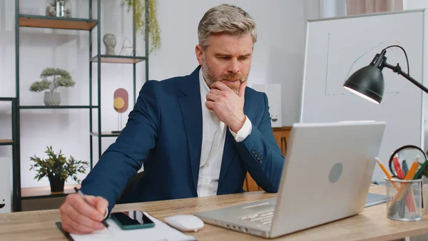 Stressed mature man feeling worried about problem analyzing information, read business papers prepare financial report at office. Freelancer frustrated thinking of money debt, budget loss bankruptcy