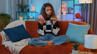 Para transfer ederken kredi kartı ve akıllı telefon kullanan küçük bir kız. İnternetten alışveriş yapıyor. Evde yemek siparişi veriyor. Genç çocuk, çocuk kanepede oyun odasında