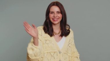 Come here, join us. Welcome. Lovely pretty woman showing inviting gesture with hands, ask to join, beckoning to coming, gesturing hello or goodbye. Young girl isolated on gray studio background