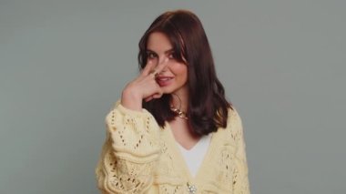 I am watching you. Caucasian woman in cardigan pointing at her eyes and camera, show I am watching you gesture, spying on someone. Young adult pretty girl isolated alone on gray studio wall background