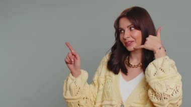 Call us, here is contact number. Young one pretty woman in cardigan looking at camera doing phone gesture like says hey you call me back, conversation. Caucasian girl isolated on gray background