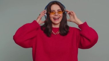 Happy pretty woman in headphones listening music and dancing disco fooling around having fun expressive gesticulating hands, relaxing on party. Caucasian girl isolated on gray studio wall background