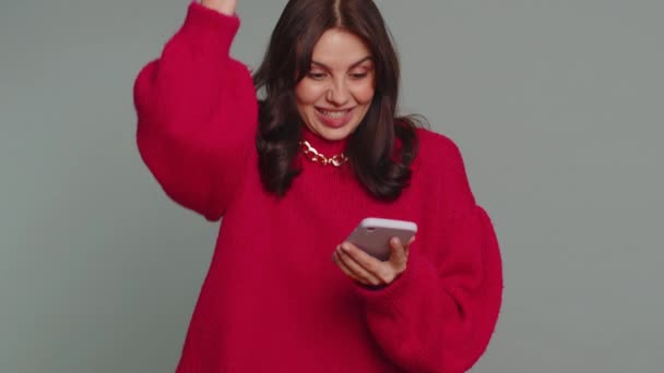 快乐快乐快乐的漂亮女人穿着毛衣用手机打字大声喊着 发现了巨大的胜利 好消息 彩票目标实现了 庆祝成功 — 图库视频影像