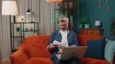 Stressed middle-aged man at home room looking at unpaid bank debt bills, doing paperwork, planning budget, calculate finances mortgage payments. Mature senior guy throws paper bills at night apartment