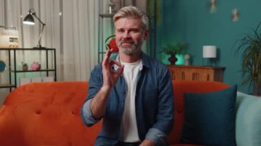 Ok. Happy cheerful middle-aged man looking approvingly at camera showing positive gesture, like sign, approve something good in living room sitting on sofa. Mature senior guy at night home apartment