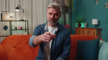 Hey you. Middle-aged old man smiling excitedly and pointing to camera, choosing lucky winner, indicating to awesome you, inviting, approve. Mature senior gray-haired guy at home night room apartment