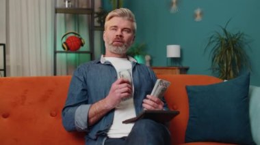Planning budget. Rich middle-aged man counting money cash use calculator and calculate domestic bills at home. Senior old guy satisfied of income earnings, win, saves money for planned vacation, gifts