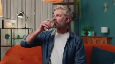 Thirsty middle-aged man holding glass of natural aqua make sips drinking still water preventing dehydration at home. Mature senior old guy with good life habits, healthy slimming, weight loss concept
