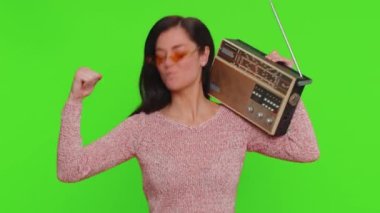 Lovely woman using retro tape record player to listen music, disco dancing of favorite track, having fun, entertaining, fan of vintage technologies. Young adult girl isolated on red wall background