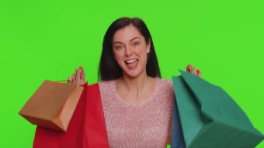 Young woman in sweater showing shopping bags, advertising discounts, smiling looking amazed with low prices, shopping on Black Friday holidays. Girl indoors isolated alone on chroma key background