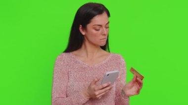Sincere woman customer using credit bank card and smartphone while transferring money, purchases online shopping, payment. Finance, internet. Young girl isolated alone on green chroma key background