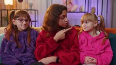 Shh be quiet please. Teen girl and little toddler child sisters presses index finger to lips makes silence gesture sign do not tell secret. Female three siblings children kids friends at home playroom